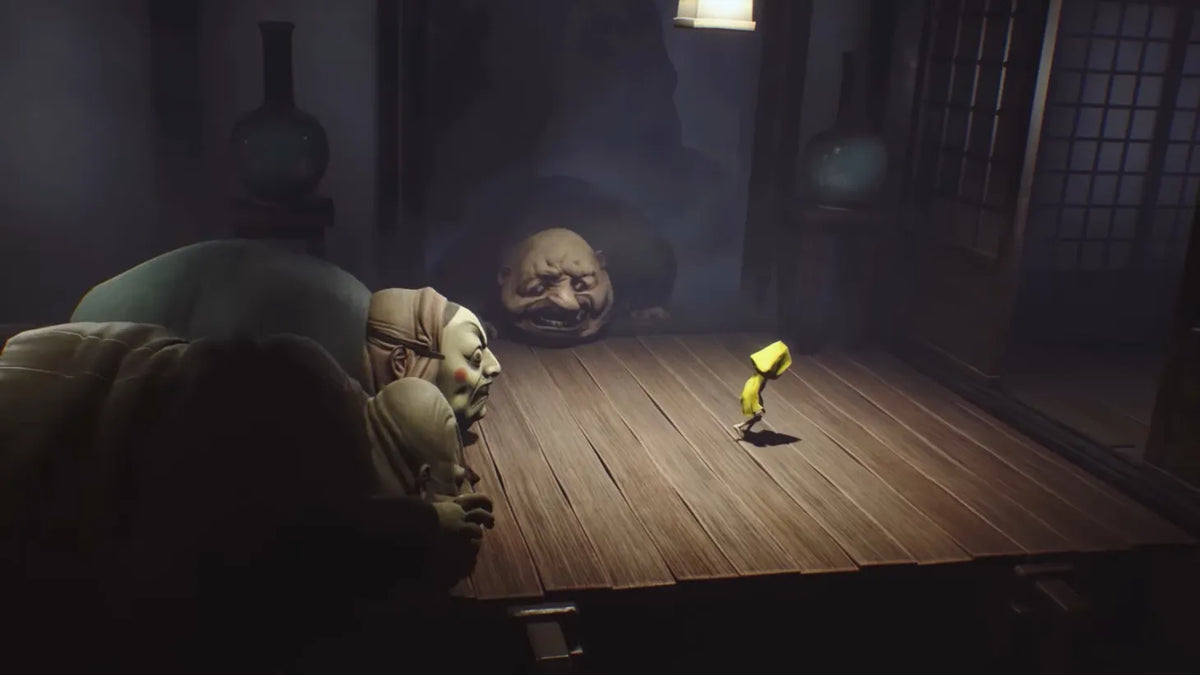Little Nightmares Enhanced Edition PlayStation 5 gameplay featuring Six in her yellow raincoat near a giant grotesque creature beside a wooden table.