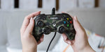 Nacon Pro Compact Forest Camo wired Xbox controller held in both hands, demonstrating its compact ergonomic shape, analogue stick positioning and gaming button layout.