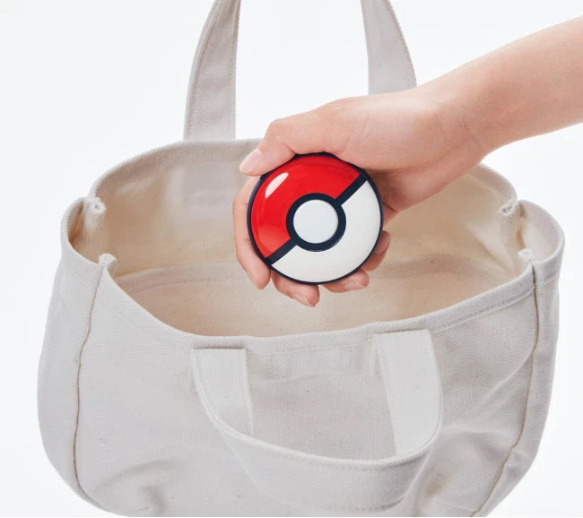 Pokémon GO Plus + Poké Ball accessory being placed into a white bag, demonstrating its compact and portable design for everyday Pokémon GO adventures.
